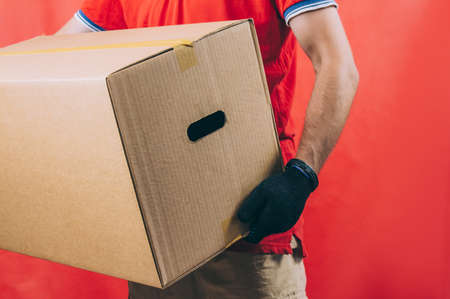 Guy with a cardboard box in his hands. Delivery service concept on red backgroundの写真素材