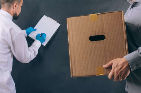 Man with a cardboard box gives a package to a client. Delivery service concept on dark background
