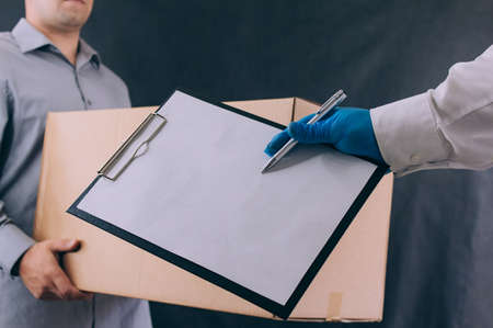 A man with a cardboard box and documents in his hands, hands over the parcel to the client. Delivery...