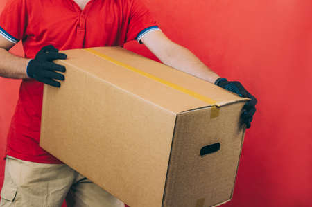 Guy with a cardboard box in his hands. Delivery service concept on red backgroundの写真素材