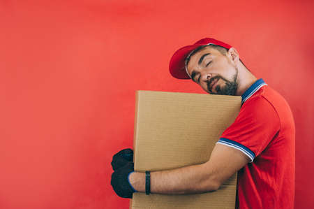 Guy with a cardboard box in his hands. Delivery service concept on red backgroundの写真素材