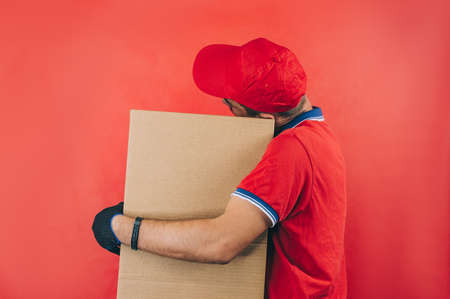 Guy with a cardboard box in his hands. Delivery service concept on red backgroundの写真素材