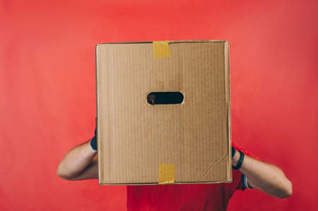 Guy with a cardboard box in his hands. Delivery service concept on red backgroundの写真素材