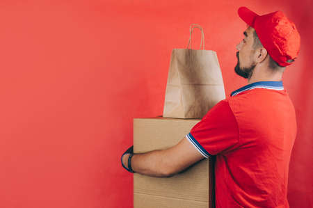 Guy with a cardboard box in his hands. Delivery service concept on red backgroundの写真素材