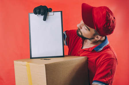 Guy with a cardboard box in his hands. Delivery service concept on red backgroundの写真素材