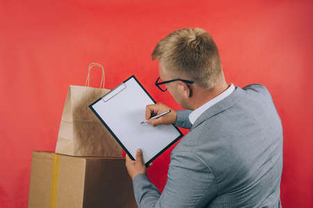 Guy with a cardboard box in his hands. Delivery service concept on red backgroundの写真素材