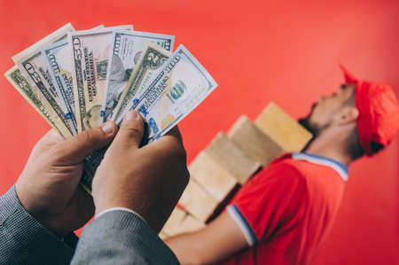 The boss pays money to his employee with dollars in hand. Concept on a red backgroundの写真素材