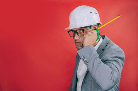 Chef in a construction helmet and a tape measure in his hands on a red backgroundの写真素材