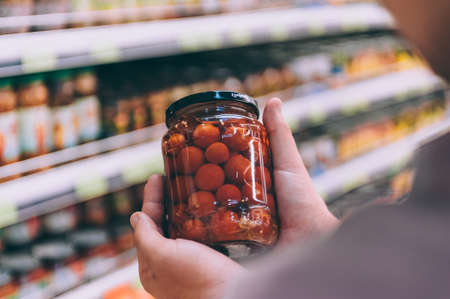The guy in the supermarket holds a glass jar with tomatoesの写真素材