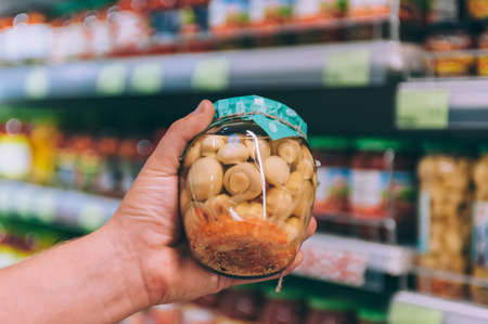 The guy in the supermarket holds a glass jar with mushroomsの写真素材