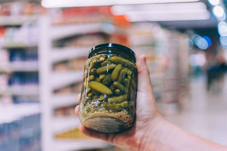The guy in the supermarket holds a glass jar of cucumbersの写真素材