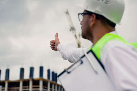 Chief in a vest and a construction helmet with documents in his hands, against the background of a...