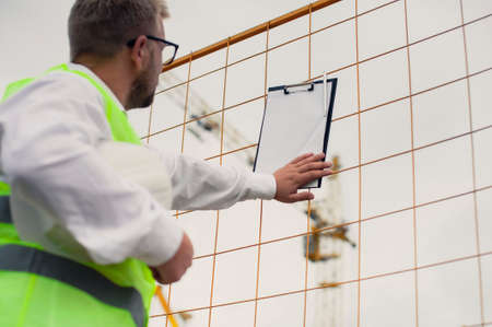 Chief in a vest and a construction helmet with documents in his hands, against the background of a tower crane and the sky with clouds. House construction inspectionの写真素材