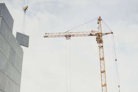 Tower crane for building houses on the background of a panel house and cloudsの写真素材