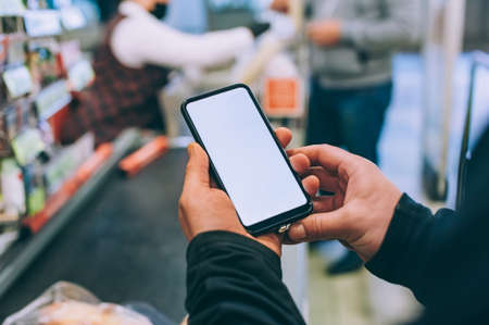 The guy is holding a smartphone with a white screen in the storeの写真素材