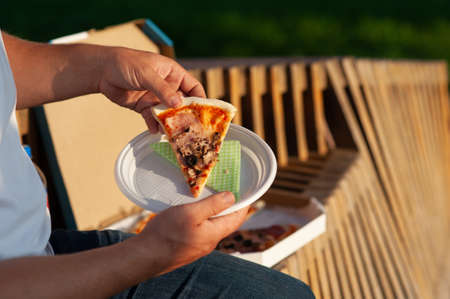 The man on the bench is eating pizza. Fast food in the fresh airの写真素材