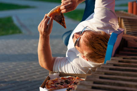 The man on the bench is eating pizza. Fast food in the fresh airの写真素材