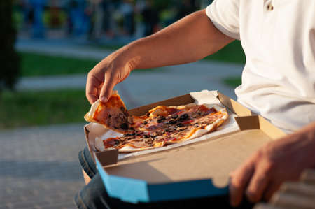 The man on the bench is eating pizza. Fast food in the fresh airの写真素材