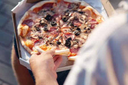 A man holds a slice of pizza in his hands. Fast food in the fresh airの写真素材
