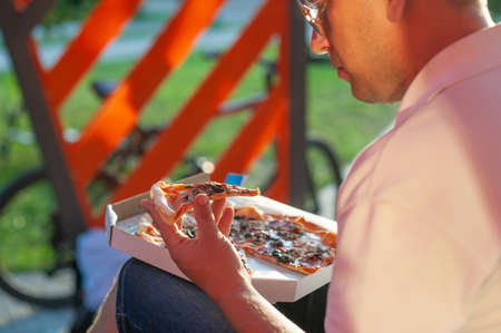 A man holds a slice of pizza in his hands. Fast food in the fresh airの写真素材