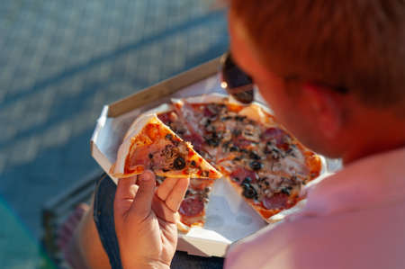 A man holds a slice of pizza in his hands. Fast food in the fresh airの写真素材