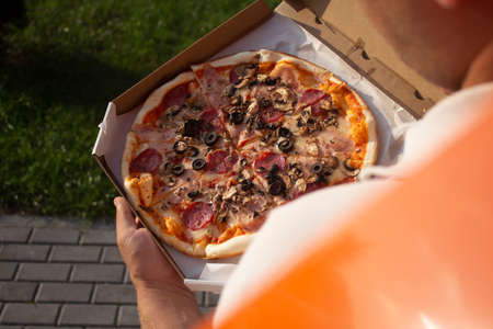 A man holds a box of pizza in his hands. Fast food in the fresh airの写真素材