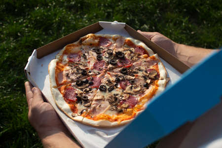 A man holds a box of pizza in his hands. Fast food in the fresh airの写真素材