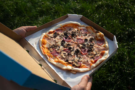 A man holds a box of pizza in his hands. Fast food in the fresh airの写真素材