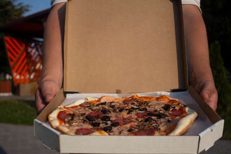 A man holds a box of pizza in his hands. Fast food in the fresh airの写真素材