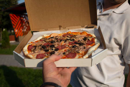 A man holds a box of pizza in his hands. Fast food in the fresh airの写真素材