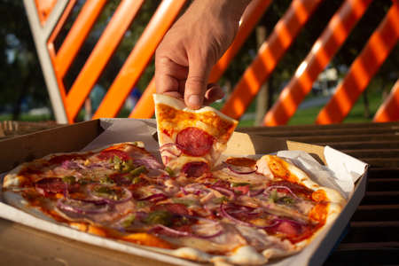 A man holds a slice of pizza in his hands. Fast food in the fresh airの写真素材
