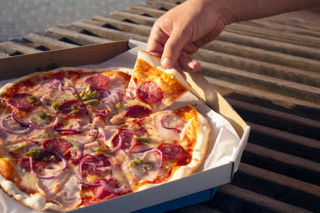 A man holds a slice of pizza in his hands. Fast food in the fresh airの写真素材