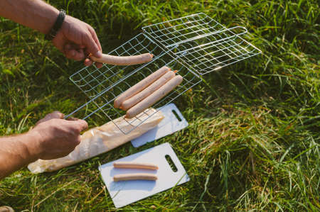 The guy puts sausages on the wire rack. Picnic in natureの写真素材