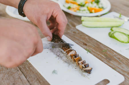 The guy cuts sausages on the background of fresh vegetable saladの写真素材