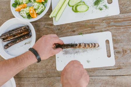 The guy cuts sausages on the background of fresh vegetable saladの写真素材