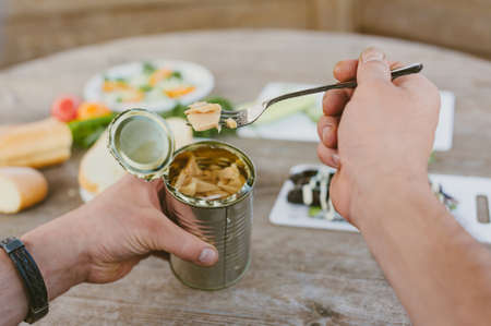 The guy eats mushrooms from a jar at the table against the background of plates with salad