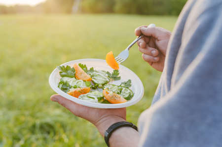 Picnic in nature. The guy is holding a plate with fresh vegetable saladの写真素材