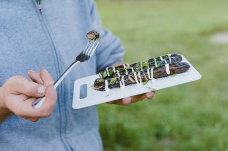 Picnic in nature. The guy is holding a tray with grilled sausagesの写真素材