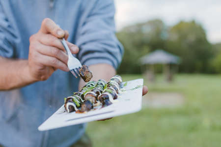 Picnic in nature. The guy is holding a tray with grilled sausagesの写真素材