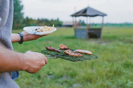 Picnic in nature. The guy holds in his hands a plate with mushrooms and meat on the grill on the background of natureの写真素材