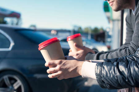 The girl with the guy at the gas station drinks coffee on the background of the carの写真素材