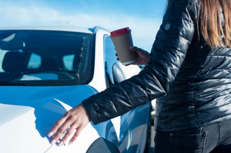 The girl drinks coffee with a glass in her hand on the background of the carの写真素材