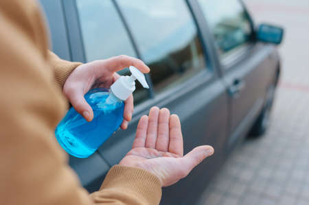 A man disinfects his hands in a parking lot with a car in the backgroundの写真素材
