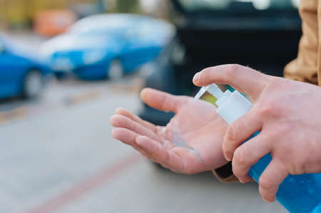 A man disinfects his hands in a parking lot with a car in the backgroundの写真素材