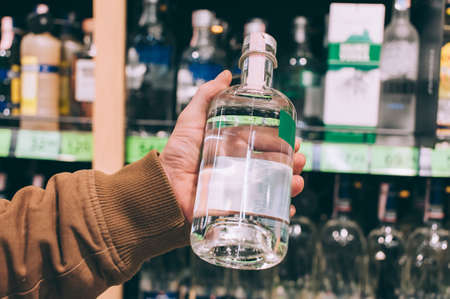 A male shopper in a supermarket holds a bottle of vodka in his handsの写真素材