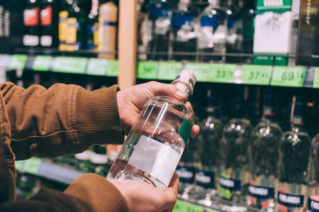 A male shopper in a supermarket holds a bottle of vodka in his handsの写真素材