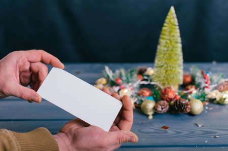 A man holds a postcard on a background with decoration on a wooden table. Festive composition for new year and christmasの写真素材