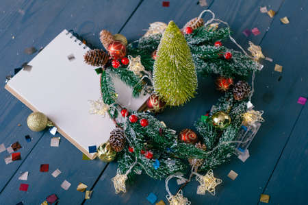 Festive composition for new year and christmas. Notepad on the background of a Christmas tree with decoration on a wooden tableの写真素材