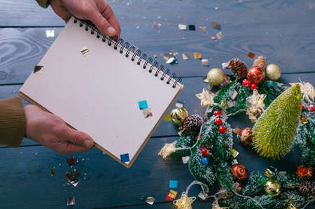 A man holds a notepad on a background with decoration on a wooden table. Festive composition for new year and christmasの写真素材