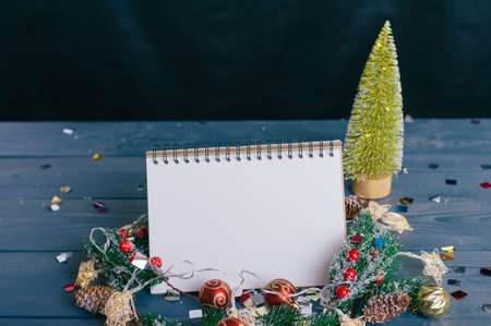 Festive composition for new year and christmas. Notepad on the background of a Christmas tree with decoration on a wooden tableの写真素材